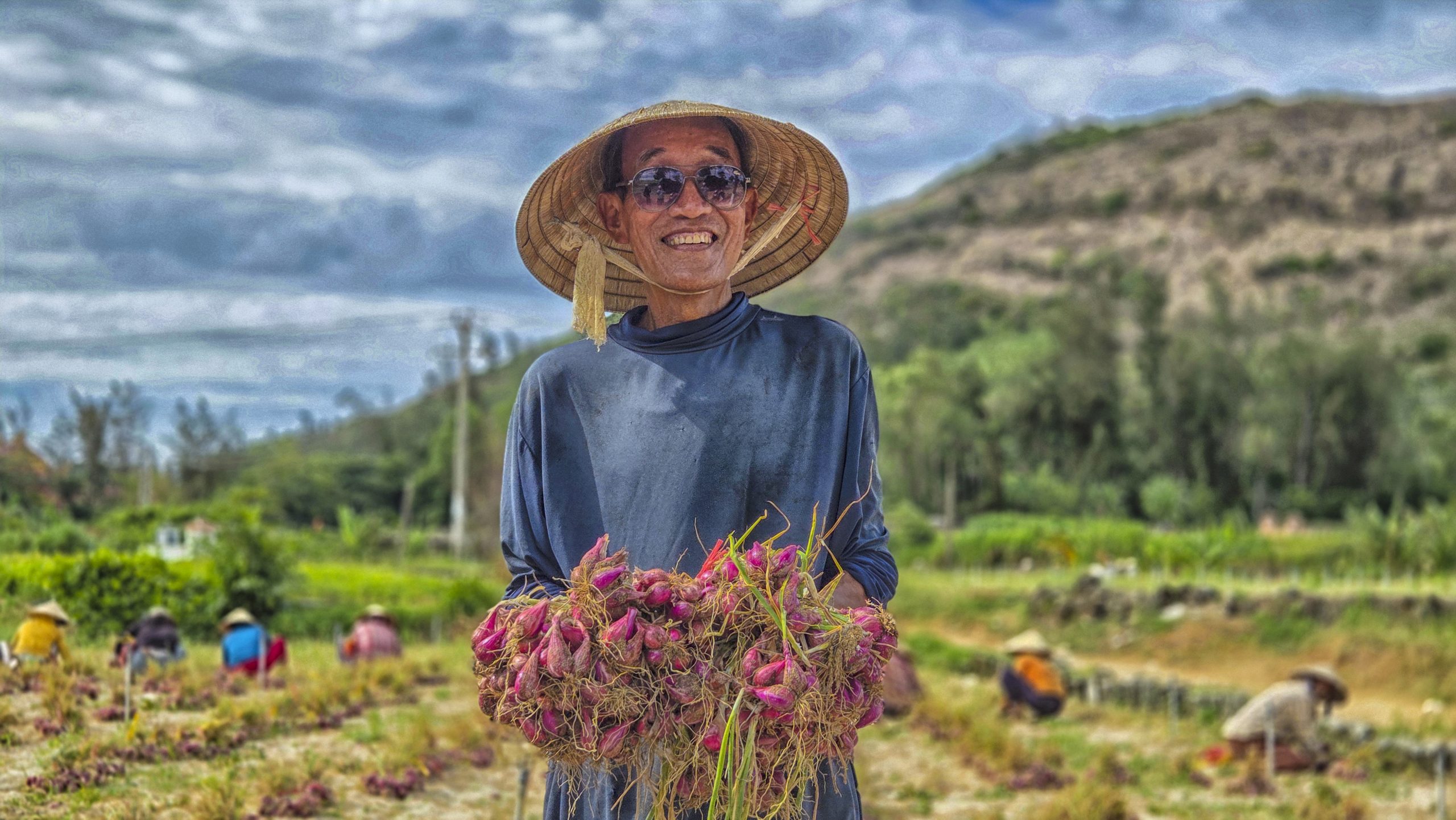 Nụ cười vui nhộn của người nông dân Lý Sơn bên những bó hành tím vừa thu hoạch.